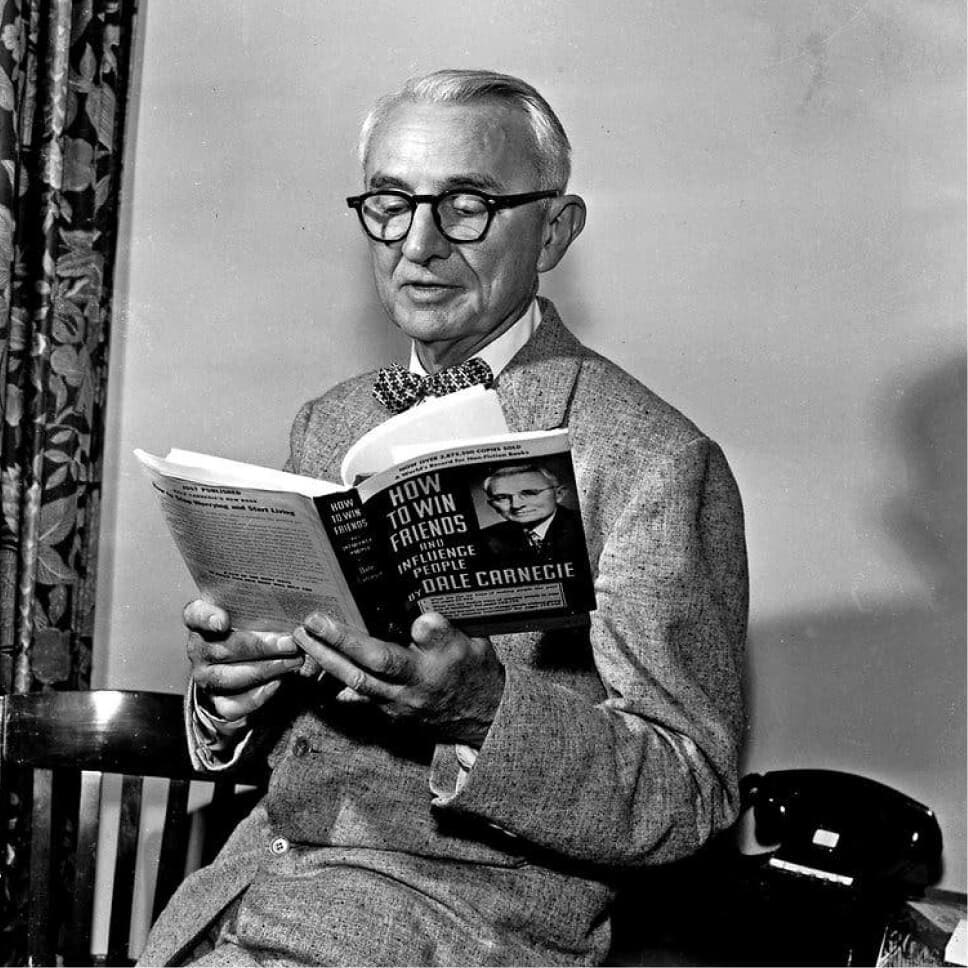 Foto em preto e branco do autor Dale Carnegie lendo seu livro Como fazer amigos e influenciar pessoas