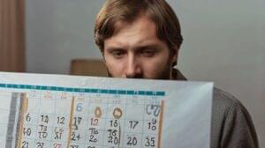 Homem jovem olhando o calendário com expressão compenetrada